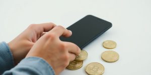 Person holding phone, looking at crypto coins.